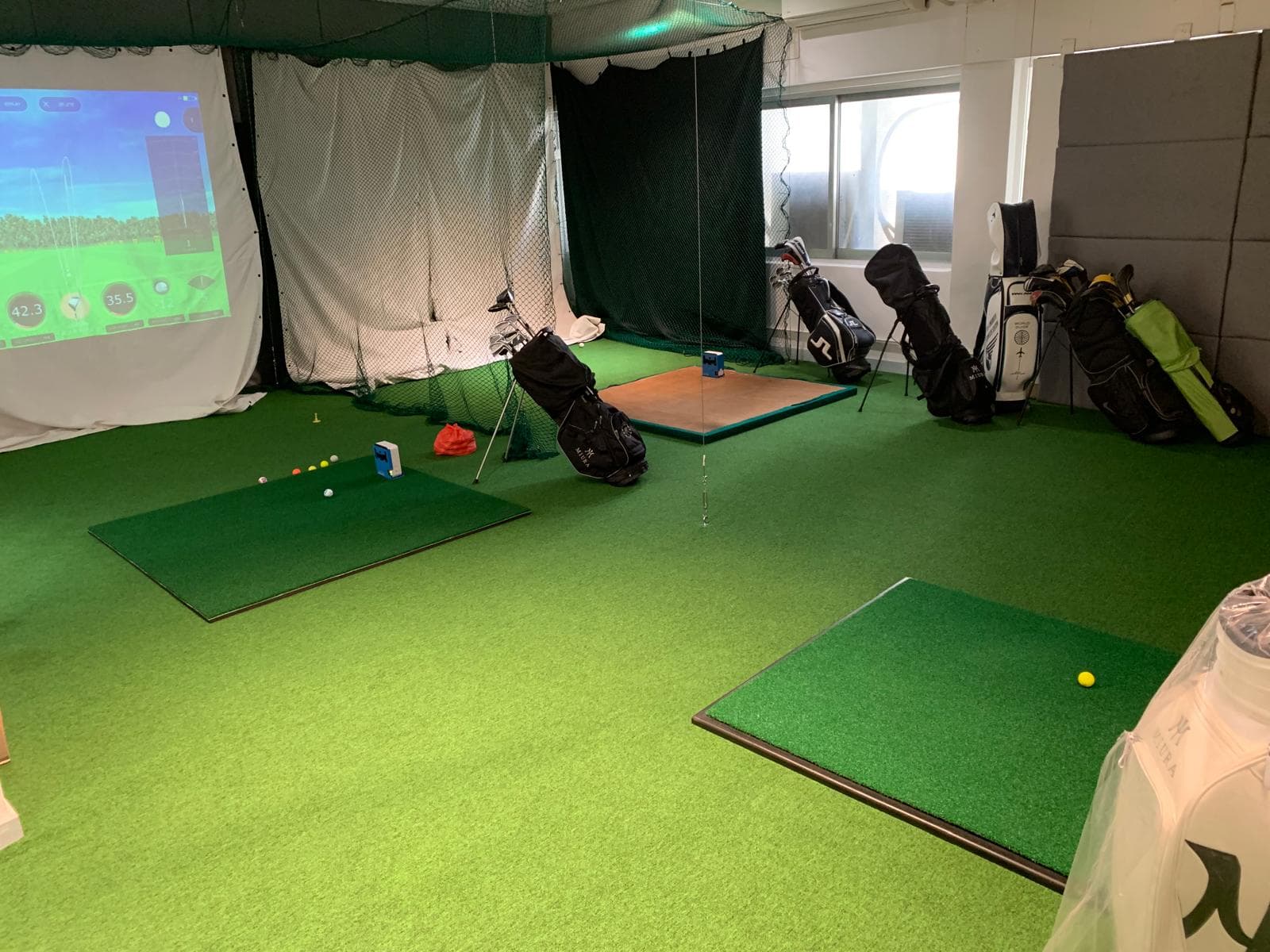 Practice area with simulator screen and golf bags at Golf Partners